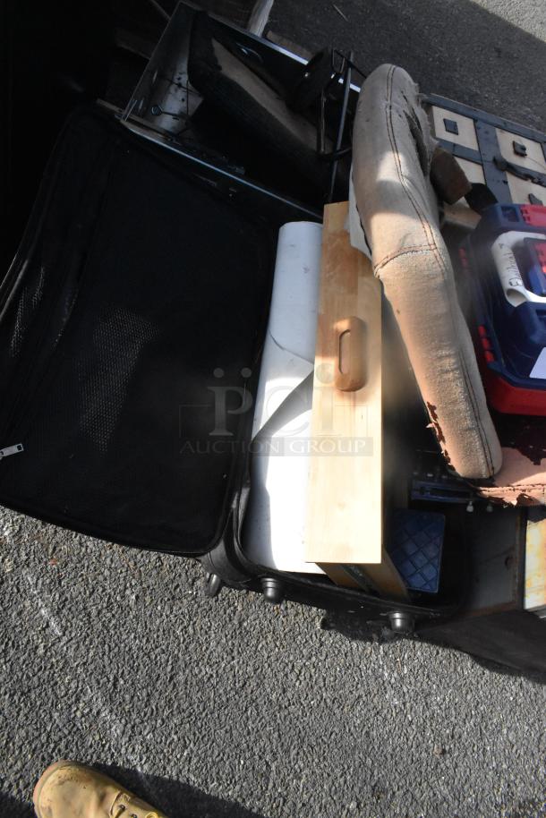 Various items including seat cushions and a wooden piece, placed in a black suitcase on pavement. Visible wear on cushion.
