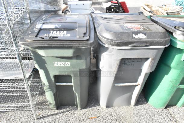 Two poly trash cans with hinged lids and sturdy handles. One green labeled U2892159, one gray with faded writing. Used condition.