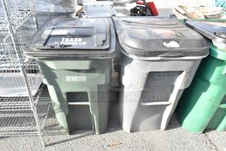 Two poly trash cans with hinged lids and sturdy handles. One green labeled U2892159, one gray with faded writing. Used condition.