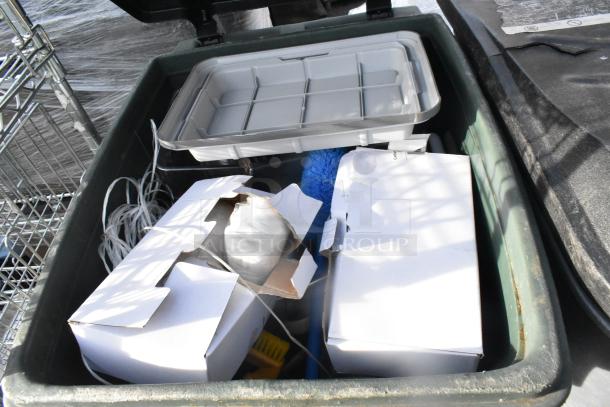 Green poly trash can filled with various items, including boxes and a tray. Used condition, no visible brand markings.