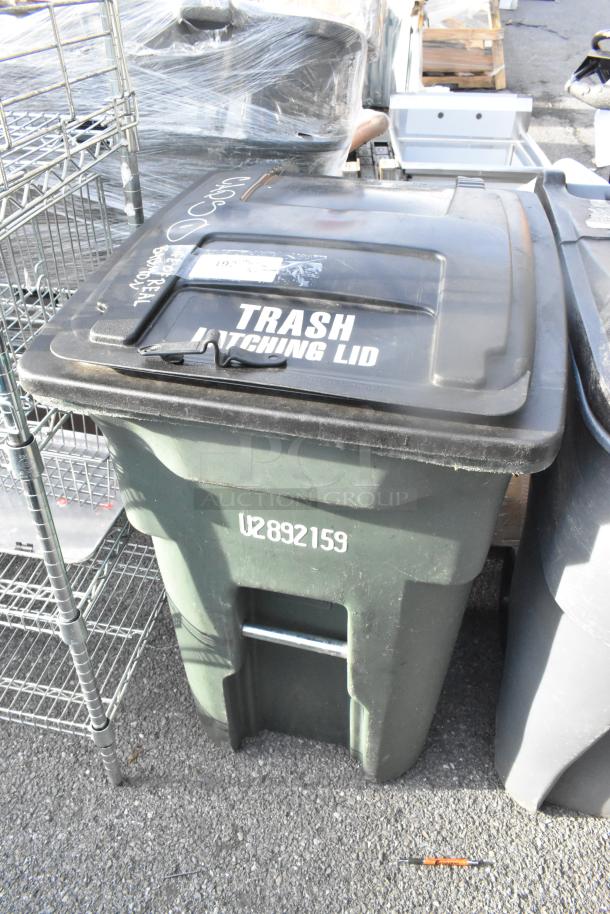 Two green poly trash cans with black latching lids, labeled "Trash Latching Lid" and marked "U2892159." Condition: used.
