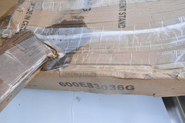 Damaged cardboard box marked "Equipment Stand," showing signs of scratches and dents. Contains Steelton Sink, Regency Equipment Stand.