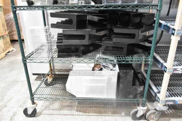 Two-tier metal cart with poly lid dispensers and a clear plastic bin, showing visible wear, stacked on green shelves.