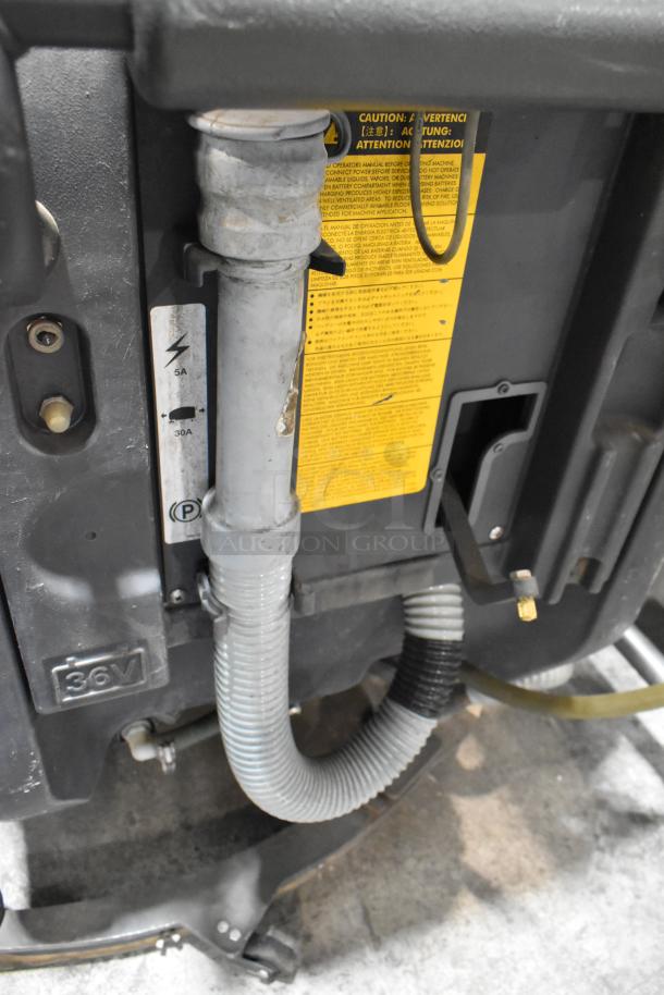 Nilfisk Advance floor cleaning machine; visible hose and caution label; model details indicate 36V power requirement.