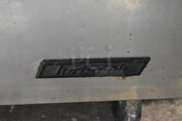 Turbo Air TST-48SD-D2 stainless steel prep table label, showing signs of wear, mounted on commercial casters.
