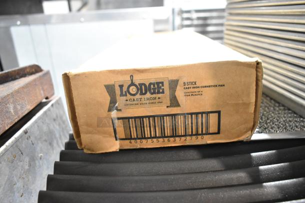 Box of 4 Lodge Cast Iron Cornstick Pans, new condition, featuring 9 stick design. Box labeled with Lodge branding and item code L927C3.