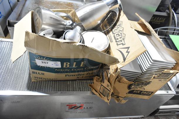 Lot of metal pitchers and stacked ceramic plates in worn cardboard boxes. Boxes labeled "Blue Nitrile Exam Gloves" and "Coors Light."