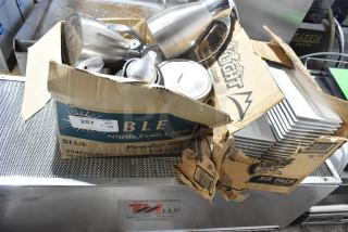 Lot of metal pitchers and stacked ceramic plates in worn cardboard boxes. Boxes labeled "Blue Nitrile Exam Gloves" and "Coors Light."