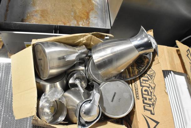 Box of assorted items including metal pitchers and ceramic plates, featuring Lignum brand markings on lids, in good condition.