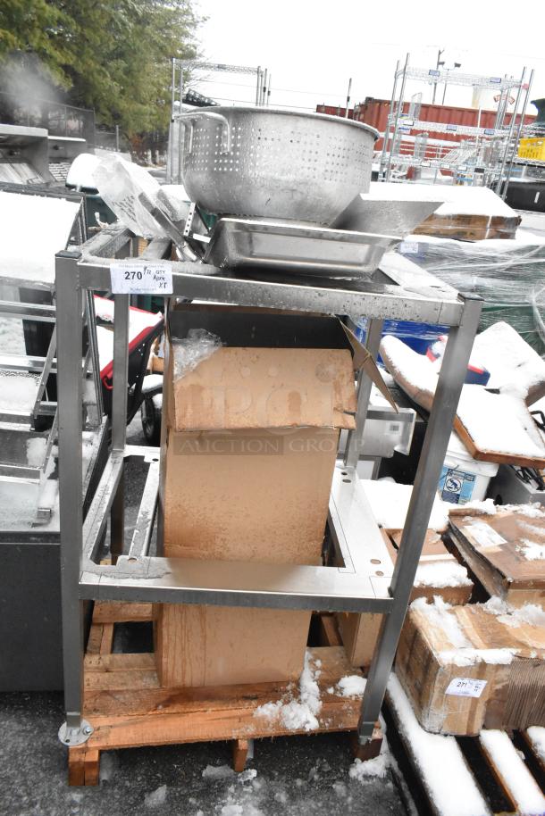 Assorted kitchen items including a metal colander, drop-in bin, and metal pan rack on a pallet, lightly used.