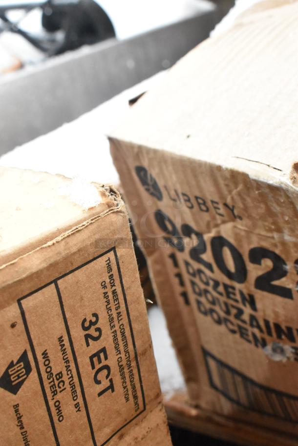 Boxes labeled Libbey 920284 and 32 ECT, containing new scratch-and-dent items, including Regency speed rail and Monin syrup rack.