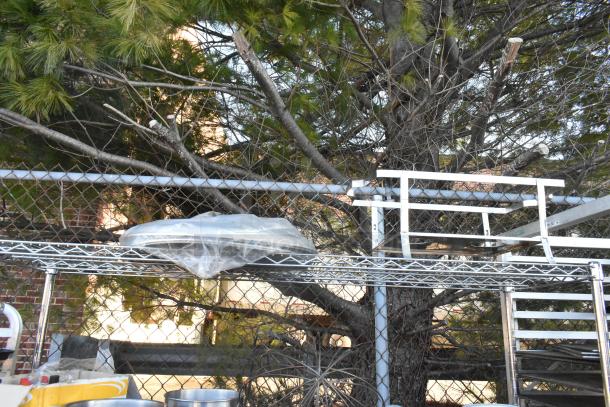 Chrome finish 4-tier wire shelving unit with contents including a chafer, mixing bowls, whisk attachments, and skillets. Buyer must dismantle.