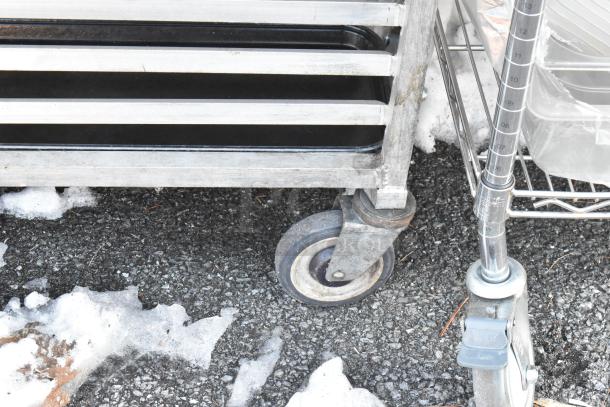 2 metal commercial pan transport racks with sturdy commercial casters, slightly worn, ideal for kitchen use.