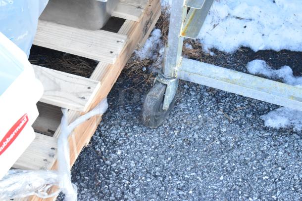 Alt text: Metal pan transport rack on casters, used condition, shown on wooden pallet.