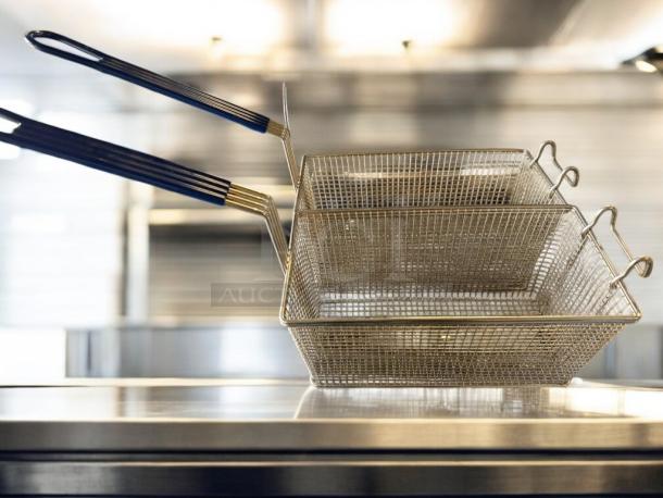 Two metal fryer baskets with black handles resting on a stainless steel surface.