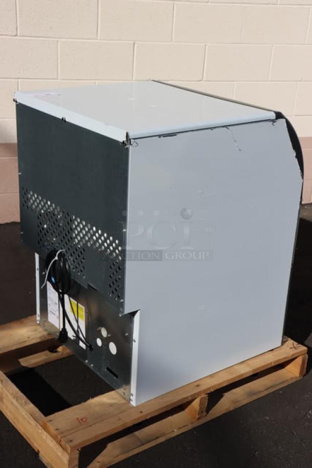 BRAND NEW Scotsman UC2024MA-1 ice machine on wooden pallet. Minor dents and scratches visible. Includes power cord and label with serial number.