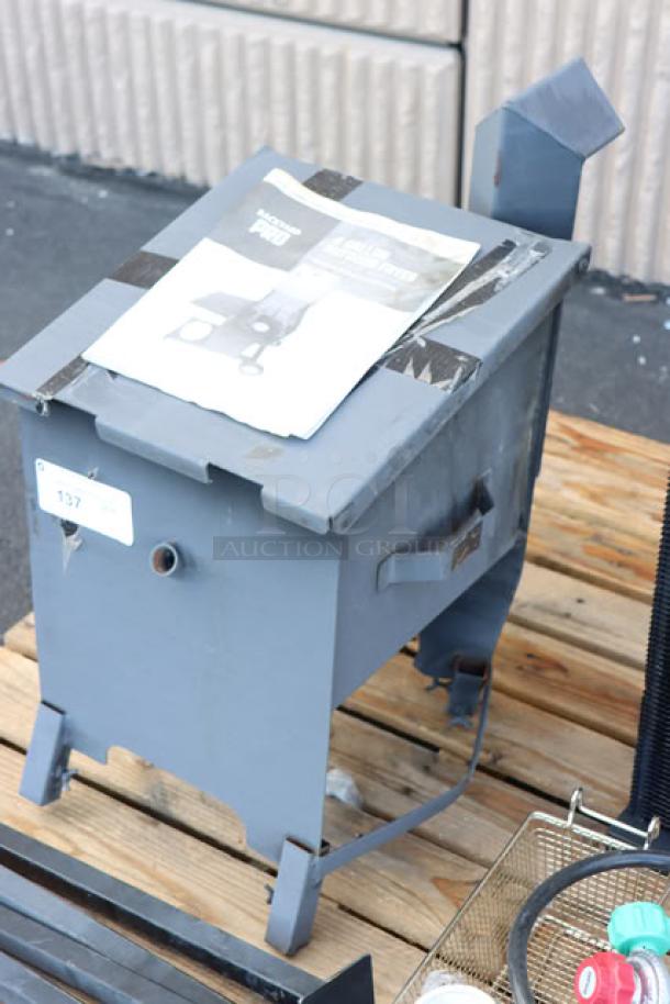 Steel deep fryer component on a pallet, blue paint, taped manual on top. No visible brand markings.роль