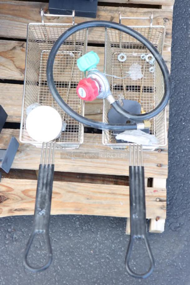 Two metal frying baskets with black handles on a wooden pallet, featuring a propane regulator and hose. Brand new, missing packaging.