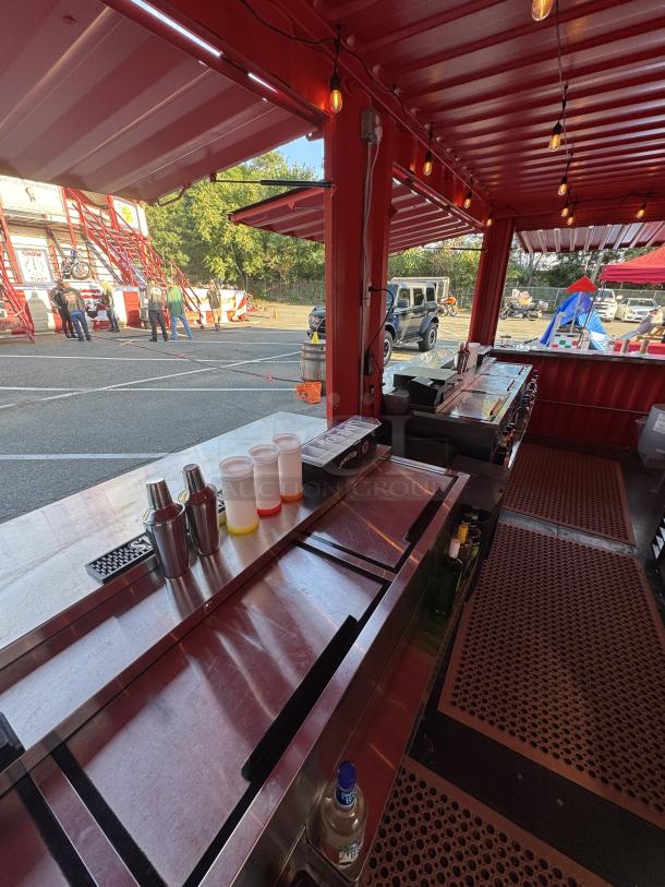 Custom "Sandlot Beach Bar" container interior with high-end bar equipment, string lights, and vibrant red design.