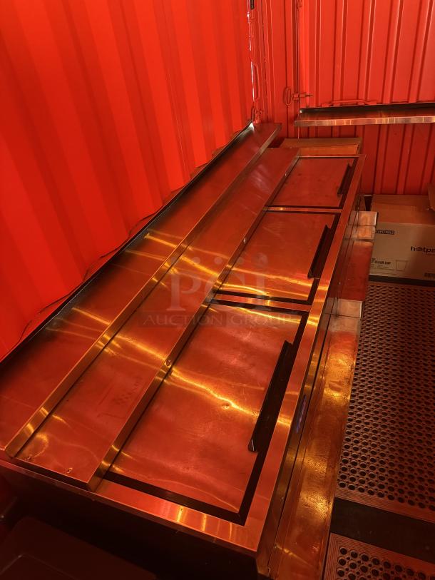 Custom mobile beach bar container interior with stainless steel surfaces. Features built-in storage and vibrant red walls.