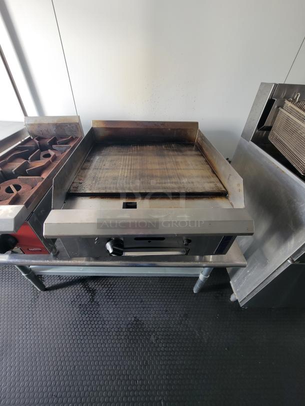 Commercial kitchen with a flat top griddle, dual grate grill, and fryer in a mobile food trailer. Non-slip floor visible.