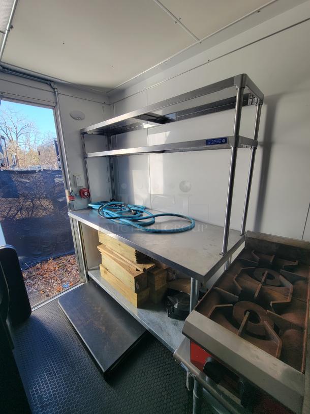 Interior of a 2021 Covered Wagon mobile food trailer with prep tables, metal shelves, and a dual grate grill.