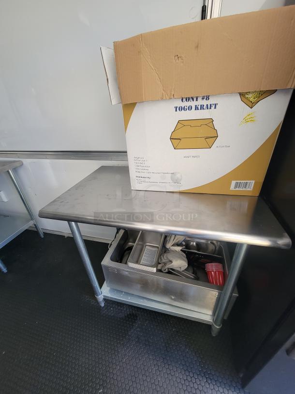 Stainless steel prep table with a cardboard box labeled "TOGO KRAFT" on top, located inside a mobile food trailer.