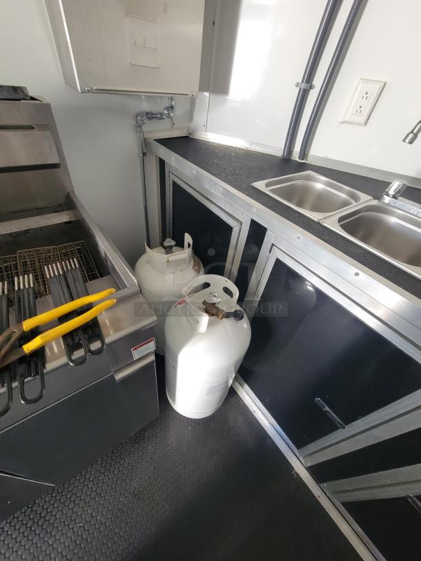 2021 16' mobile food trailer interior with dual Anets SLG40 fryers, two propane tanks, and part of a 4-compartment sink.