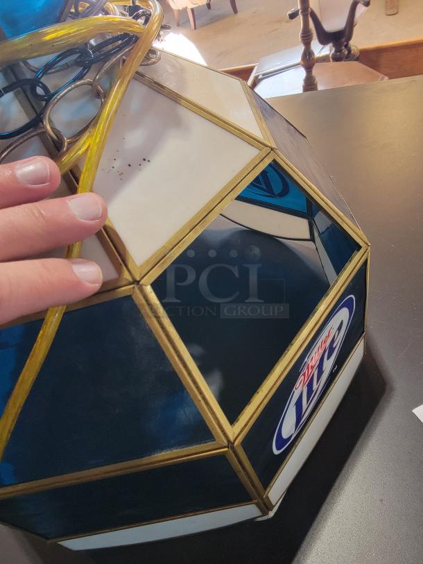 Vintage Miller Lite Tiffany-style stained glass pendant light with brass-tone frame, showcasing iconic branding. One light visible with blue and white pattern; part of a set with two in excellent condition and two with glass damage.