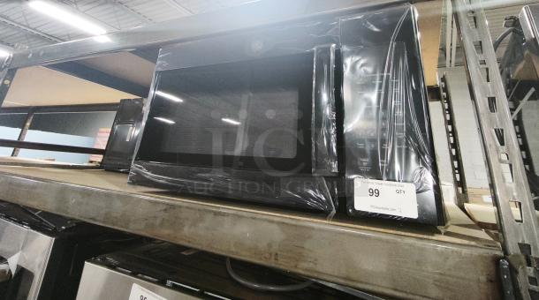 BRAND NEW GE 1.6 Cu. Ft. Over-the-Range Microwave Oven, Model JVM3160DF9BB, wrapped in protective plastic, on auction shelf.