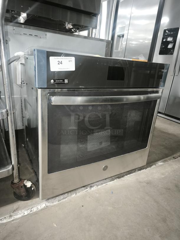 Brand new stainless steel oven, model GE, with glass door. Auction lot tag reading "24 QTY". Mint condition.