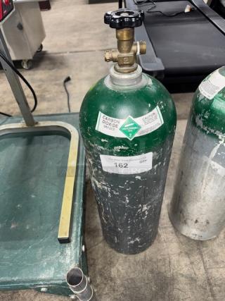 60 cuft aluminum oxygen cylinder with a green top, visible wear and markings, labeled with hazardous material warnings.