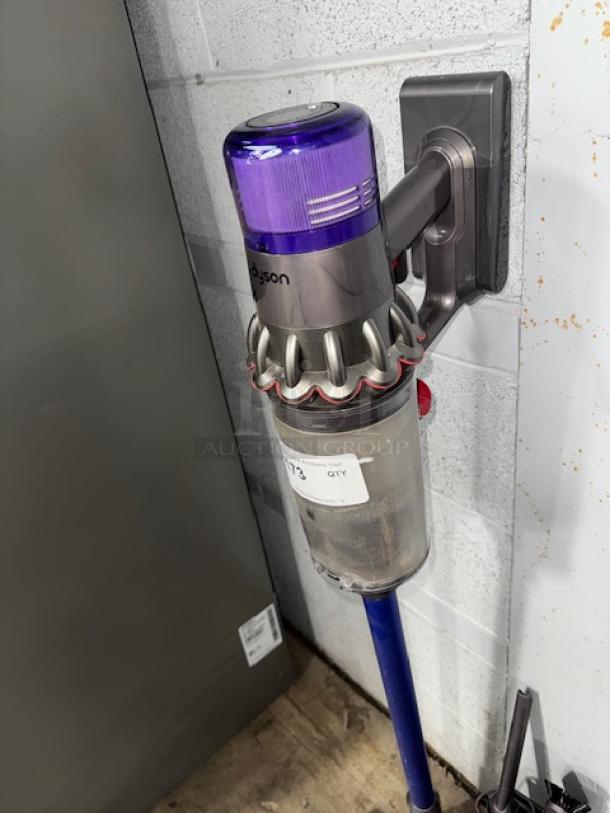 Dyson V11 Torque Drive+ cordless vacuum in good condition, mounted on a wall charger. Dustbin appears partially filled.