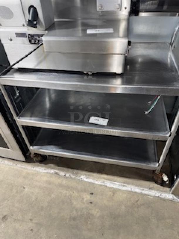 Stainless steel service cart, 31 x 19 x 33 inches, featuring three shelves with minor wear, caster wheels, labels on shelves.