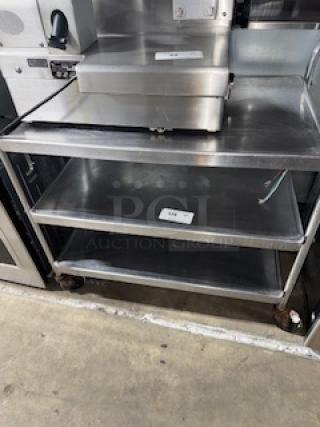 Stainless steel service cart, 31 x 19 x 33 inches, featuring three shelves with minor wear, caster wheels, labels on shelves.