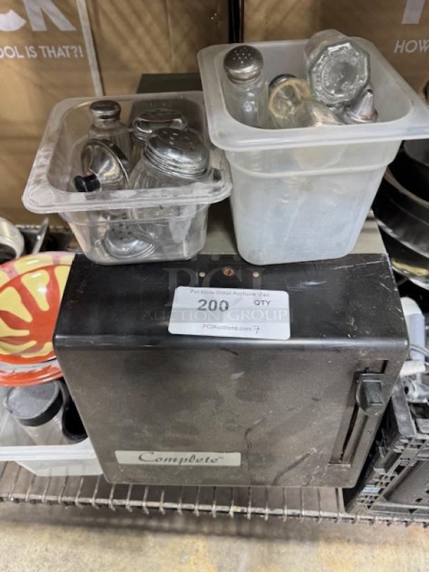 Plastic bins with assorted metal shakers and bottles atop a black Complete brand dispenser. Label reads "200 QTY."