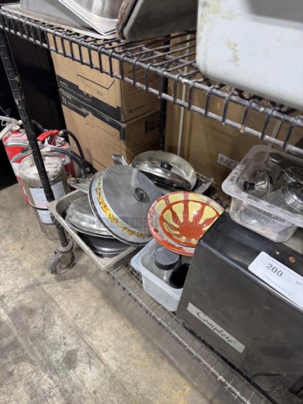 Assorted kitchenware on a metal shelf, includes pots, lids, and a decorative bowl. Items show signs of use. All one price.