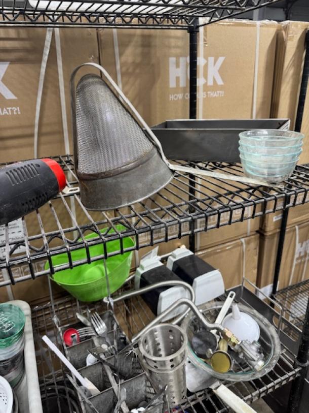 Collection of assorted kitchenware on metal shelves, including mesh strainer, glass bowls, and baking pan. Items in used condition.