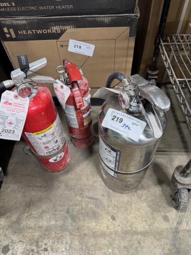 Three Class ABC fire extinguishers, one red, two silver; tagged 218, 219; used condition with visible instructions.
