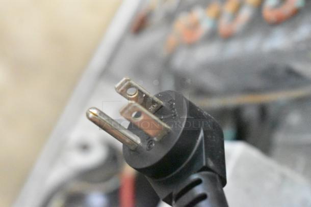 Close-up of a plug from a Delfield 406P-STAR2 cooler, focusing on the prongs and black casing, indicating 115V power compatibility.