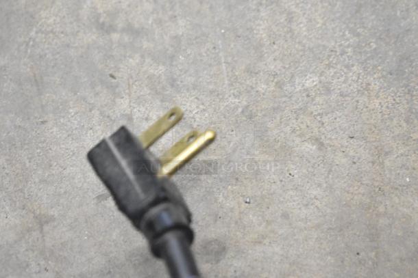 Blurred image of a two-prong electrical plug against a concrete background.
