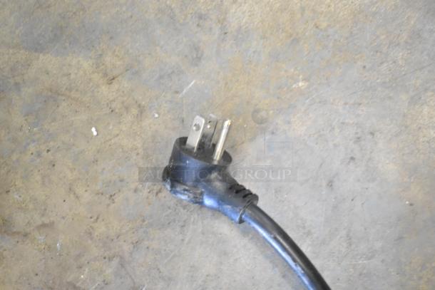 The image shows a black electrical plug on a concrete floor, possibly part of the True T-19F-HC freezer.
