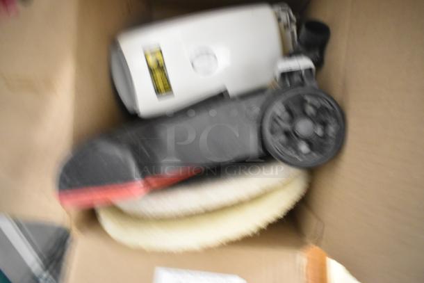 Box containing various items including a white appliance with a black wheel and cord, condition unclear.
