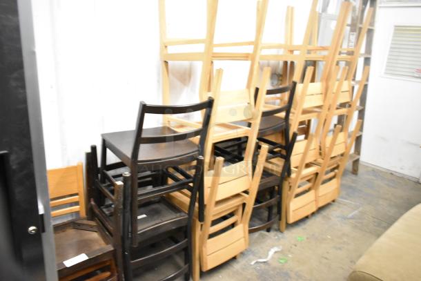 16 assorted wooden dining chairs in various shades, stacked. Good condition. Ideal for bulk purchase or event seating.