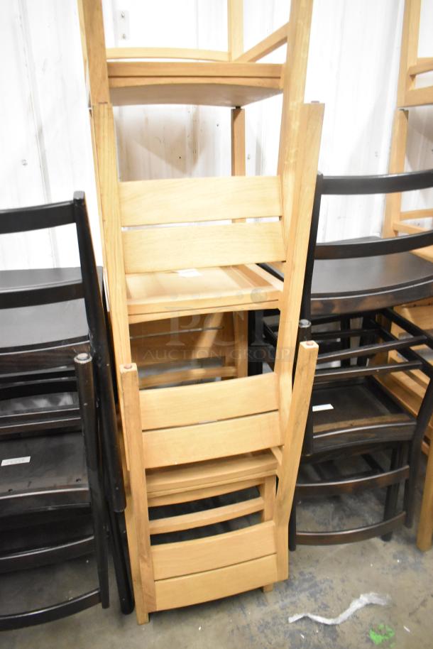 16 assorted wooden dining height chairs, natural and black finishes, stacked in a storage setting, appear well-maintained.