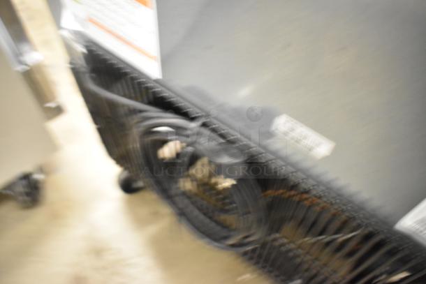 Blurry image of the back of a stainless steel True T-23F-HC commercial freezer, showing coils and electrical plug.