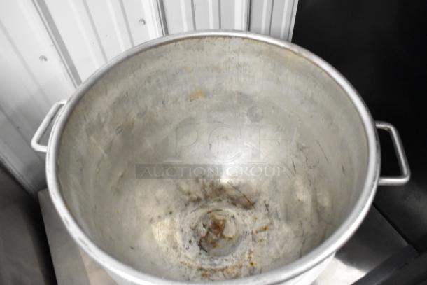 Large metal mixing bowl with handles, showing signs of wear with visible scratches and discoloration, suitable for heavy-duty use.