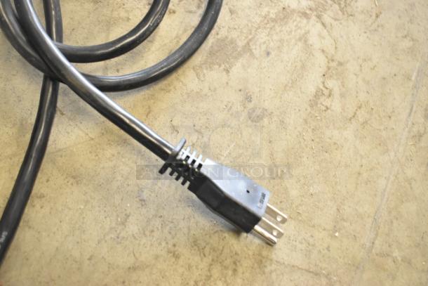 Power cord of 2023 Bizerba GSE 12 Meat Slicer, 110 volts, 1 phase, showing standard three-prong plug on concrete surface.