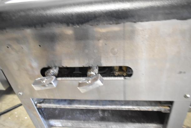 Stainless steel commercial countertop gas burner range with dual control knobs, showing signs of use and wear.