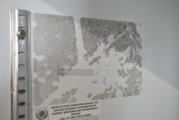 Beverage Air commercial cooler interior with worn metal surface and warranty label indicating contact information.